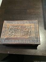 Closed walnut rectangular trinket box with carved lid showing floral or leaf motif and geometric border detail.
