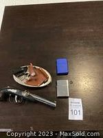 Overview of lot on table showing flintlock pistol, leather holster, belt buckle, and two Zippo lighters (blue and silver)