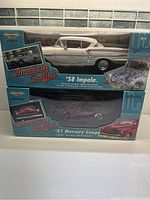 Front view of the unopened boxed set showing two model cars from American Graffiti, the '58 Impala in white and the '51 Mercury Coupe in red, with visible signatures on packaging.