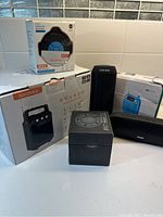 Photo showing six Bluetooth speakers with some boxed and unboxed items, including different brands and styles.