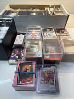 Overview of two storage boxes filled with assorted cards, plus stacked cards in top loaders and rubber-banded bundles.