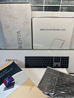 Lot of wireless keyboard boxes and two keyboards in packaging with accessories and manuals for keyboard cases.