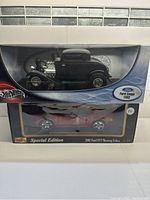 Two die cast cars in original packaging, a black 1932 Ford Coupe by Hot Wheels on top and a red 2003 Ford SVT Mustang Cobra by Maisto below.