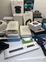 Photo showing over 20 boxes of digital watches and fitness trackers including Bugani V5 wireless headset box and various smart bracelet boxes.