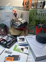 Photo showing various boxed and unboxed home and electronic items including Omega Tree Stand, Nintendo Switch Lite box, small electronics and accessories.