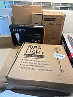 Photo showing boxed ring fill light, Shellkingdom desk lamp box, 4-pack of LED filament bulbs, and other boxed lighting items in background.