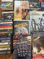 Lot including various DVDs, VHS tapes, and cassette tapes showing titles such as 'Die Hard 2', 'Muppets from Space', 'Rollerball', along with music cassettes.