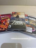 Photo of three Nintendo Switch game cases: The Legend of Zelda: Breath of the Wild, Rocket League Collector's Edition, and Giana Sisters: Twisted Dreams Owltimate Edition, arranged side by side on white surface.