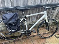 Full left-side view of white Cannondale Quick 5 hybrid bike with black rigid fork and mounted black Axiom pannier bag