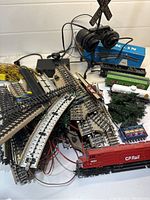 Multiple vintage Lionel train cars including red CP Rail locomotive, coal car, boxcar, tank car, set on various curved and straight metal train tracks with wiring.