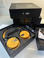 Open box showing yellow Cowin E7 Pro wireless headphones with auxiliary cable in foam packaging.