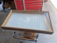 Top angled view of the wooden display case with glass lid open, showing the white slatted interior and natural wood frame.