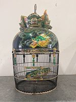 Full view of the birdcage showing the painted dragon dome, sculpted dragon top, and metal cage sides.
