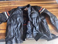Photo of front side of black leather Harley Davidson jacket showing style, zippers, and stripes.