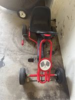 Front view of the red and black pedal cart with crossed checkered flags emblem on front, plastic seat, and tires visible.