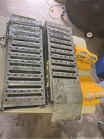 Full view of two metal loading ramps on a table with four yellow plastic wheel chocks in the background and a fan nearby.