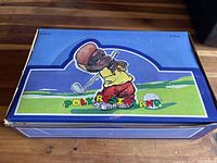 Closed vintage polyresinland box with colorful illustration of a cartoon-style golfer in red pants and yellow shirt on the lid, labeled 'Polyresinland'.