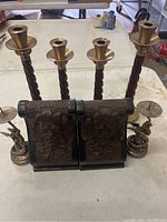 Photo showing four twisted wood and brass candleholders with some patina, a pair of carved wood bookends with floral and leaf relief, and two small dragon-shaped metal candleholders.