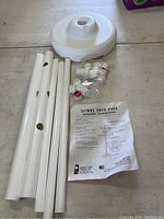 Photo showing four white tubular poles, white weighted base, a set of plastic caps with red tips, and the assembly instruction sheet for Towel Tree #401.