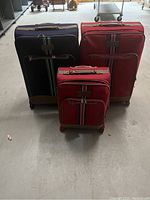 Photo showing all three suitcases in the set: one dark blue large, one red large, and one red small suitcase.