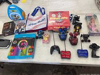 Overview of assorted toys including board game, CD player, LED light, multiple remote control cars, Play Ball tote, and small toys.
