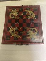 Folded wooden chess board showing red and black squares with gold dragon designs and latch closure, slight scratches visible.