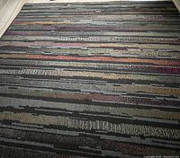 Photo of the striped design area rug with horizontal multi-color lines in varied shades including gray, beige, red.