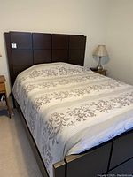 Front view of queen bed frame with decorative bedding showing headboard design with square panel grid.