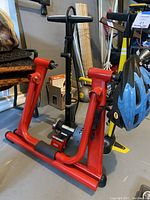 Red Ascent bike trainer stand with a black bike helmet hanging on it and a black bike pump behind it.