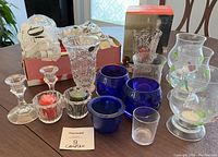 Various candles, candle holders including blue glass votives and clear glass holders with 3D decorative insects and leaves.