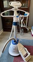 Full front view of the white and blue clothes steamer showing hanger arms, base unit, flexible hose, and steam head with power cord wrapped around