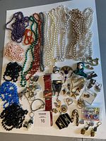 Full layout of vintage Bulova watch, bead necklaces, assorted rings, pins, earrings, and ring watch on white surface