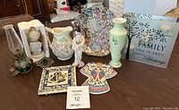 Full lot view of decorative items including plates, pitcher, vase, figurine, lamp, coasters, and glass plaque