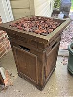 View of the full propane fire pit showing the wood finish exterior, geometric carved pattern, and lava rocks in the burner.