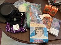 Photo showing black top hat, purple and black striped costume garment, white/light wig, vampire wig packaging, and Halloween decorations and soaps on table.