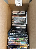 Stacked DVDs and Blu-rays inside a cardboard box showing titles and cases from various movies including Disney and other films.