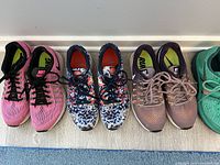 Five pairs of women's Nike Air Pegasus running shoes, size 9, in a row on the floor, showing various color options from left to right including pink, multi-color, purple, teal, and coral.