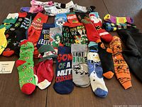 Photo displaying an array of assorted holiday novelty socks including Christmas, Halloween, and winter designs spread on a wooden surface.