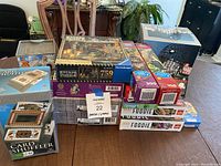 Photo showing the full lot including stacked puzzle boxes, card shuffler box, bingo cage set box, and a box of magic cards.