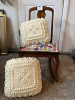 Front view of the small antique wooden rocking chair with two cushions placed on the seat and one cushion leaning on the chair back.