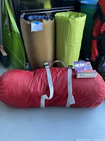 Two bed rolls, one brown and one green, positioned upright behind the tent bag.