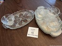 Photo showing four clear glass snack plates and four matching punch cups on a wooden table, displaying the grape cluster and leaf pattern.