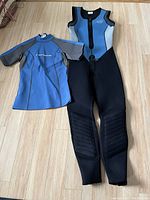 Two-piece women's wet suit set laid flat on floor, showing sleeveless vest with pants and short sleeve top, blue, grey, black colors.