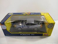 Silver die cast Porsche 911 model in original yellow and blue packaging showing front and side view through window display.