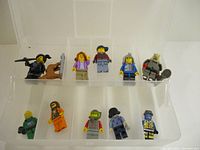 Side view of 10 assorted LEGO mini figures in plastic case compartments with better lighting.