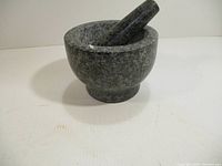 Angled side view showing the marble mortar with pestle resting inside, displaying the shape and size of the set.
