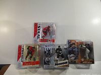 Four sports figure collectibles in plastic packaging, three hockey figures and one baseball figure.
