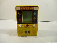 Front view of yellow mini Pac-Man handheld electronic game showing LCD screen displaying maze and Pac-Man characters, joystick and buttons.