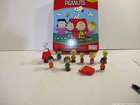 Front view of Peanuts My Busy Book with 12 character figures and playset items arranged in front of the book