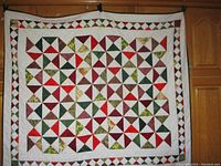 Full view of handmade quilt with patchwork triangular pinwheel design in reds, greens, browns, and cream.